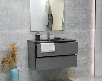 May include: A gray bathroom vanity with two drawers and a black countertop. The vanity has a white towel hanging on the front. There is a mirror above the vanity and a vase with dried flowers on the floor.
