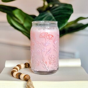 May include: A glass with a pink floral design filled with a pink beverage. The glass is sitting on a stack of books with a wooden bead garland.