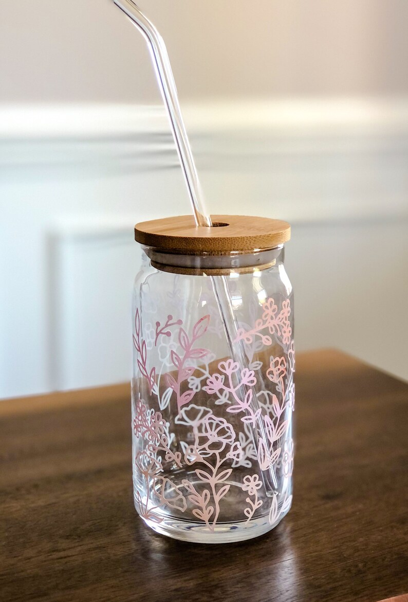 May include: A clear glass jar with a bamboo lid and a pink floral design. A clear glass straw is inserted through the lid.