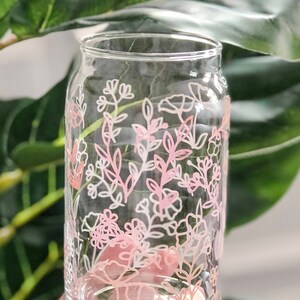 May include: A clear glass drinking glass with a pink and white floral design. The design features delicate flowers and leaves.
