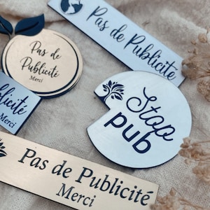 May include: A collection of rectangular and circular signs in gold and silver tones. The signs feature black text including Pas de Publicite, Merci, and Stop pub, along with small tree and globe icons. These decorative plaques are designed for display.