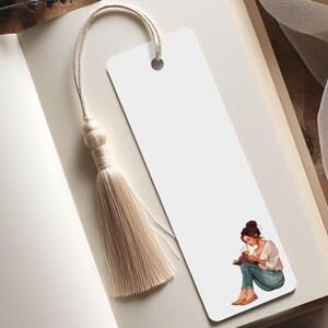 K&ouml;nnte beinhalten: Ein wei&szlig;es Lesezeichen mit einer beigen Quaste, das in einem offenen Buch liegt. Das Lesezeichen zeigt eine Illustration einer lesenden Person. Die Seiten des Buches sind cremefarben.