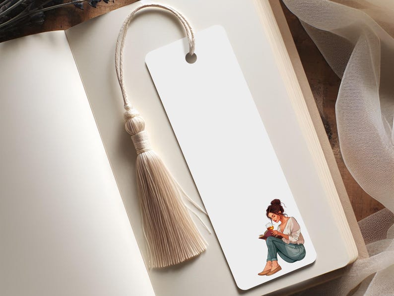 K&ouml;nnte beinhalten: Ein wei&szlig;es Lesezeichen mit einer beigen Quaste, das in einem offenen Buch liegt. Das Lesezeichen zeigt eine Illustration einer lesenden Person. Die Seiten des Buches sind cremefarben.