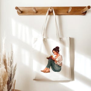 K&ouml;nnte beinhalten: Eine wei&szlig;e Tragetasche mit einer Grafik einer Frau, die ein Buch liest und ein Glas bernsteinfarbener Fl&uuml;ssigkeit h&auml;lt. Die Frau tr&auml;gt ein wei&szlig;es Hemd, blaue Jeans und braune Schuhe. Die Tragetasche h&auml;ngt an einem Holzregal.