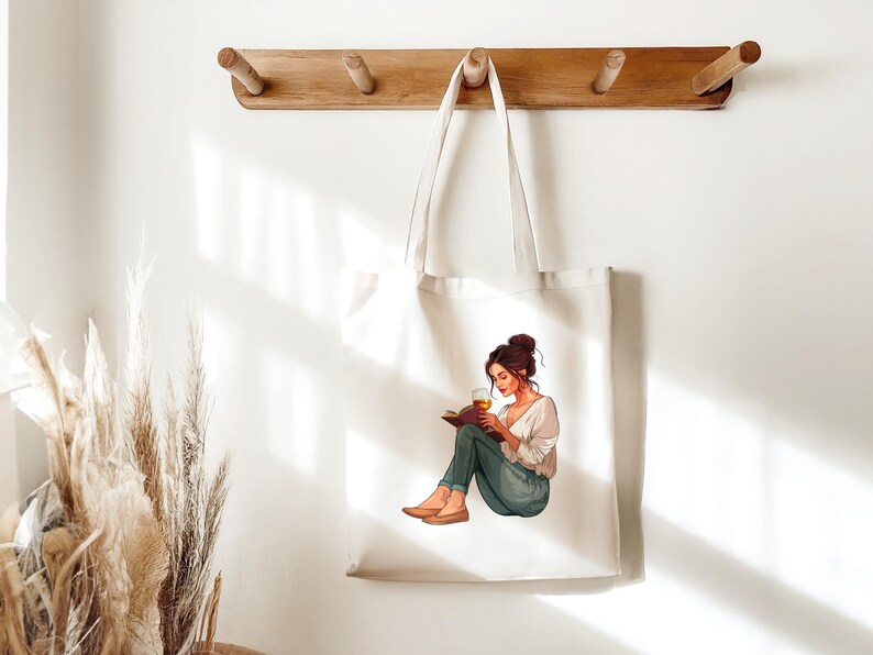 K&ouml;nnte beinhalten: Eine wei&szlig;e Tragetasche mit einer Grafik einer Frau, die ein Buch liest und ein Glas bernsteinfarbener Fl&uuml;ssigkeit h&auml;lt. Die Frau tr&auml;gt ein wei&szlig;es Hemd, blaue Jeans und braune Schuhe. Die Tragetasche h&auml;ngt an einem Holzregal.
