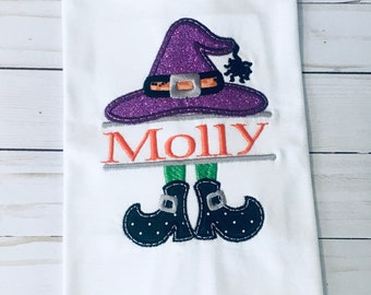May include: White t-shirt with an embroidered witch design. The witch has a purple hat with a black spider, green legs, and black shoes. The name "Molly" is embroidered below the witch.