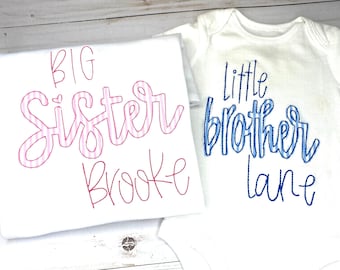 Puede incluir: Dos camisas blancas con texto bordado. La camisa más grande dice "BIG Sister Brooke" en rayas rosas y blancas. La camisa más pequeña dice "little brother Lane" in rayas azules y blancas.