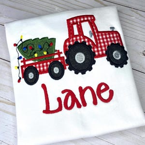 May include: Red and white gingham tractor pulling a wagon with a green Christmas tree and lights. The name "Lane" is embroidered below the tractor.