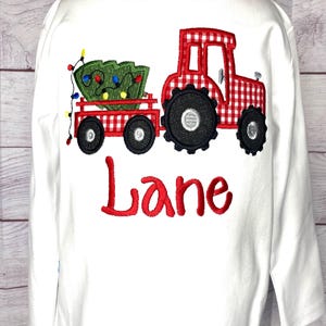 May include: White long-sleeved shirt with a red and white gingham tractor pulling a Christmas tree with lights. The name "Lane" is embroidered in red below the tractor.