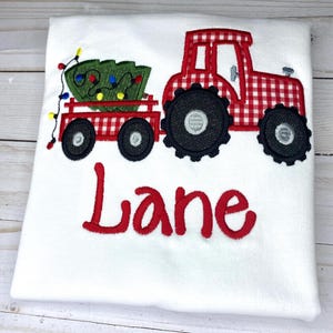 May include: Red and white gingham tractor pulling a wagon with a green Christmas tree and lights. The name "Lane" is embroidered below the tractor.