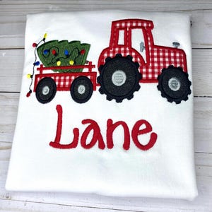 May include: Red and white gingham tractor pulling a wagon with a green Christmas tree and lights. The name "Lane" is embroidered below the tractor.