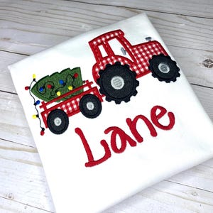 May include: Red and white gingham tractor pulling a wagon with a green Christmas tree and lights. The name "Lane" is embroidered in red below the tractor.