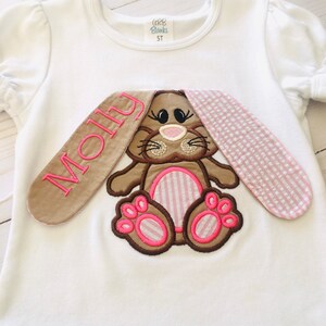 May include: White t-shirt with a brown bunny applique. The bunny has pink ears, pink paws, and a pink nose. The shirt is personalized with the name "Molly" in brown embroidery.