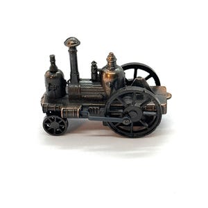 May include: A miniature antique steam engine model in a bronze finish. The model features a tall smokestack, two large wheels, and several detailed components. The overall design is reminiscent of early industrial machinery.
