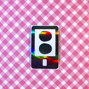 May include: A black and white sticker of a smartphone with a holographic finish. The phone screen displays a traffic light with two red circles.