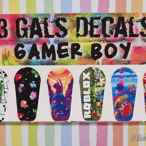 May include: A rectangular sticker sheet with the text "3 GALS DECALS GAMER BOY" above six illustrated decals. The decals feature characters from popular video games, including Minecraft, Among Us, and Roblox.
