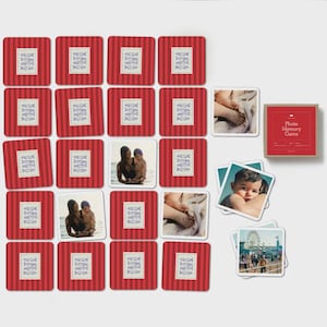 May include: A photo memory game set featuring square cards with a red and white vertical striped pattern and a central white label depicting blue fish. Some cards display personal photographs of people and feet, alongside a red storage box.
