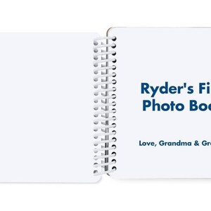 May include: A white photo album with a blue title that reads "Ryder's First Photo Book" and a blue inscription that reads "Love, Grandma & Grandpa".
