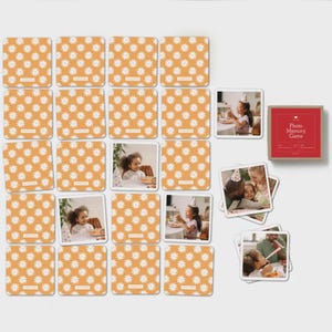 May include: A photo memory game set featuring square cards with a repeating white daisy pattern on an orange background. Some cards display photographs of children wearing party hats, and a red box is labeled Photo Memory Game in white text.