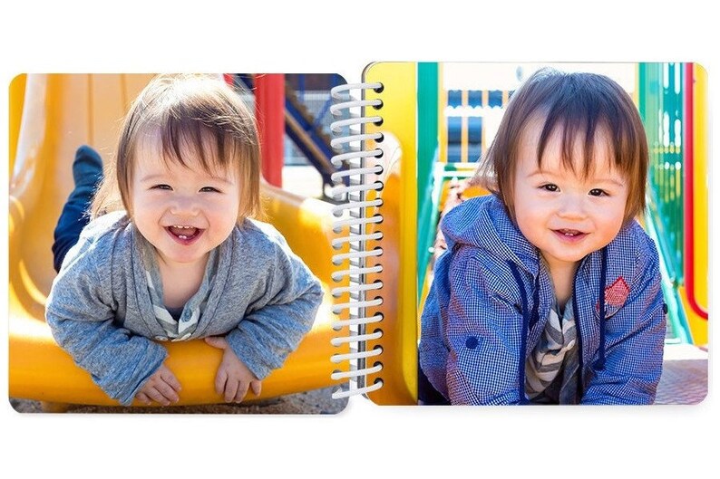 May include: Two toddlers smiling at the camera. One is on a yellow slide and the other is on a green and yellow playground structure.