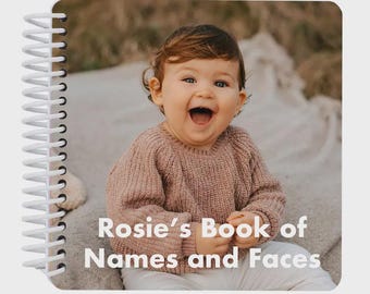 May include: A spiral-bound photo book featuring a cover image of a smiling toddler wearing a dusty pink knit sweater. The white text on the cover reads, Rosie's Book of Names and Faces, set against a soft, neutral-toned background.