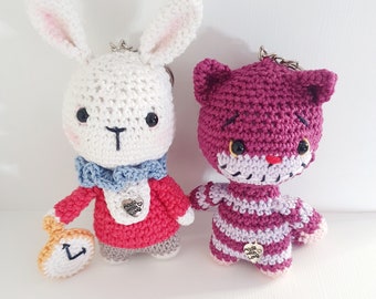 May include: Two crocheted plush toys, a white rabbit wearing a red vest and a purple cat wearing a striped shirt. Both toys have a small charm that says "Made with Love".