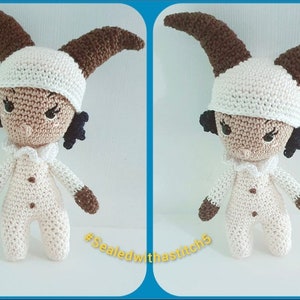 May include: A crocheted amigurumi doll with brown horns, a white hat, and a white and brown outfit. The doll has a brown face with black eyes and a serious expression. The doll is standing on a white surface. The text "#Sealedwithastitch5" is visible in the bottom right corner of the image.