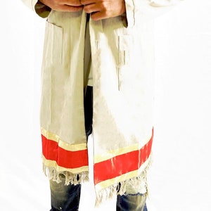 May include: A long, light beige linen jacket with a red and gold trim and fringe. The jacket has a shawl collar and a tie closure.