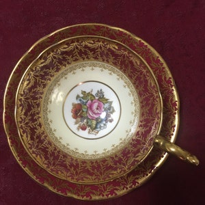 Peut inclure: Un service à thé vintage composé d'une tasse et d'une soucoupe. L'intérieur est crème avec un motif de bouquet floral. L'extérieur est rouge foncé avec des motifs de feuilles d'or et un bord doré. La poignée est dorée.
