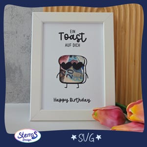 May include: White framed print with the text "Ein Toast Auf Dich" and "Happy Birthday". The image features a cartoon slice of toast wearing heart-shaped sunglasses, with a 20 Euro bill design.