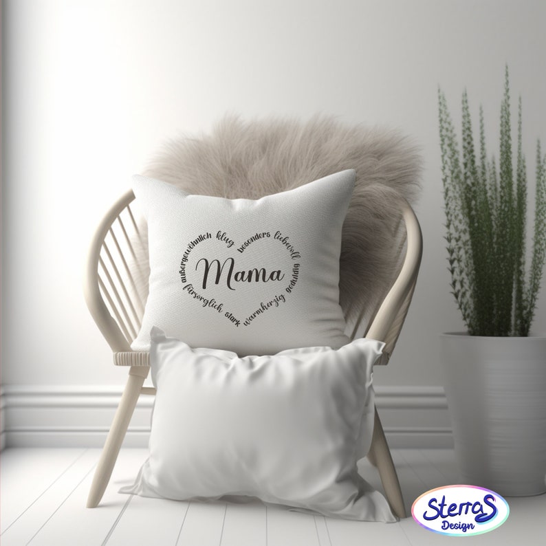 May include: White throw pillow with black text that reads "Mama" surrounded by a circle of German words. The pillow is sitting on a white wicker chair.