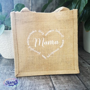 May include: A brown burlap tote bag with white text that reads "Mama" in a heart shape. The text around the heart reads "au&szlig;ergew&ouml;hnlich,  blog, besonders, liebevoll,  gef&uuml;hlvoll,  ganz,  begeisternd,  besonders,  liebevoll,  gef&uuml;hlvoll,  ganz,  begeisternd".