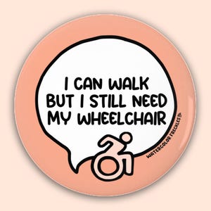 May include: A round, peach-colored button with a black border. The button features a white speech bubble containing the text "I CAN WALK BUT I STILL NEED MY WHEELCHAIR" in bold, black letters. A wheelchair symbol is below the text.
