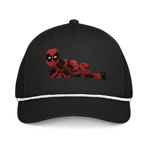 May include: A black baseball cap featuring a pixel art graphic of a red and black character lying down. The cap has a structured crown, a curved brim, and a white braided cord trim running horizontally across the base of the front panel.