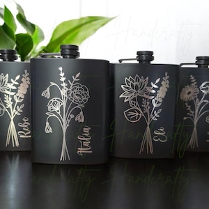 May include: Four black flasks with silver floral designs and personalized names. Each flask has a black cap and a silver floral bouquet etched on the front. The names "Rebe", "Italia", "Eli", and "Lolo" are written below the floral designs.