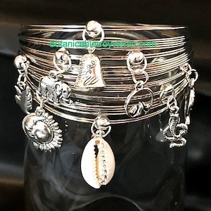 May include: A set of silver bangles with various charms, including a seashell, a sun, an elephant, a mountain, and a bell. The charms are attached to the bangles with silver chains.