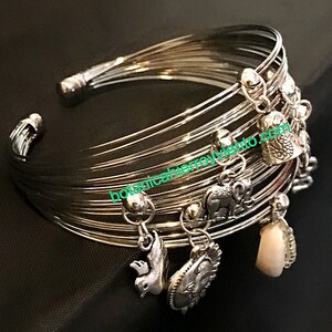 May include: Silver bangle bracelet with multiple charms, including a bird, elephant, and shell. The bracelet is made of thin, interwoven metal bands.