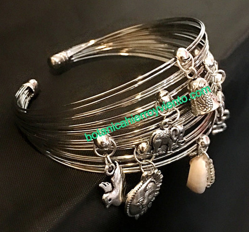 May include: Silver bangle bracelet with multiple charms, including a bird, elephant, and shell. The bracelet is made of thin, interwoven metal bands.