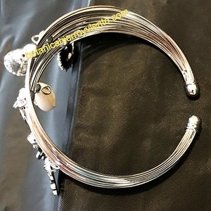 May include: Silver bangle bracelet with multiple charms, including a heart, a star, and a shell. The bracelet is made of multiple bands of metal.