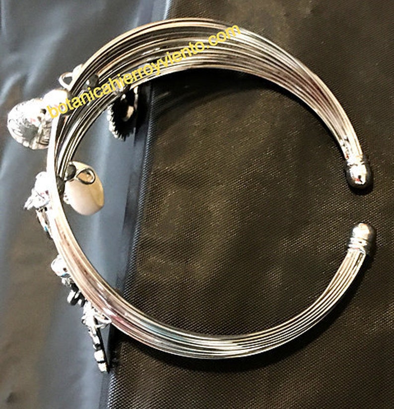 May include: Silver bangle bracelet with multiple charms, including a heart, a star, and a shell. The bracelet is made of multiple bands of metal.
