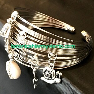 May include: A silver bangle bracelet with multiple charms, including a heart, a snail, and a bell. The bracelet is made of thin, flexible wire and has a delicate, feminine look.