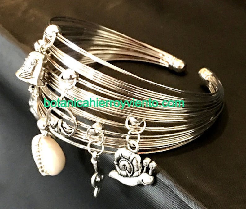 May include: A silver bangle bracelet with multiple charms, including a heart, a snail, and a bell. The bracelet is made of thin, flexible wire and has a delicate, feminine look.