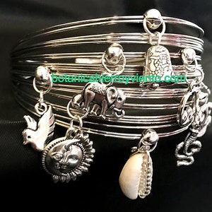 May include: Silver charm bracelet with multiple charms, including a dove, sun, elephant, seashell, and a bell with the text "botanicaherroyviento.com".