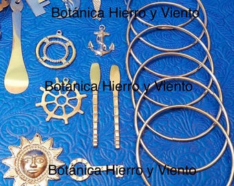 May include: A set of gold-toned metal wind chime components, including a sun, a ship's wheel, a key, a mermaid, a dolphin, an anchor, a life preserver, and two paddles. The components are arranged on a blue patterned surface. The text "Botánica Hierro y Viento" is visible in the image.
