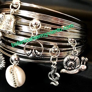 May include: Silver bangle bracelet with multiple charms, including a shell, a snail, a snake, and a tree. The bracelet is made of multiple thin silver bands.