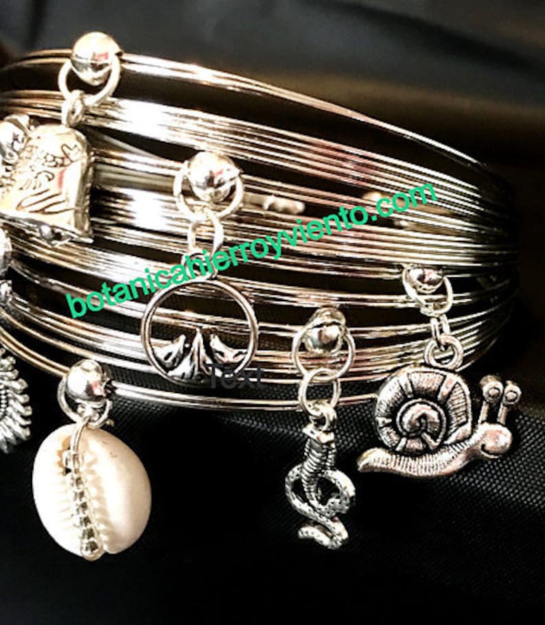 May include: Silver bangle bracelet with multiple charms, including a shell, a snail, a snake, and a tree. The bracelet is made of multiple thin silver bands.