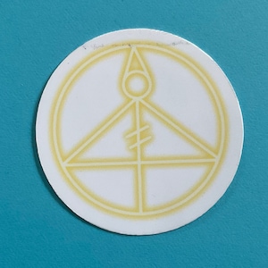 May include: A white sticker with a yellow circle and a yellow triangle inside. The triangle has a yellow line through it and a yellow circle at the top.
