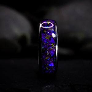 May include: A silver ring with a purple and green inlay. The inlay is made of crushed opal and is set in a smooth silver band.