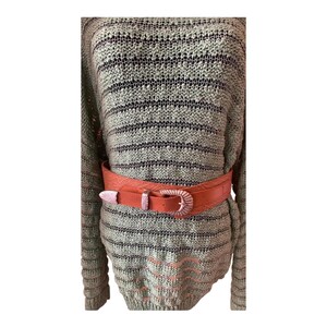 May include: A light green and black striped sweater is cinched at the waist with a wide, reddish-orange belt. The belt has a decorative silver-colored buckle. The sweater has a loose knit design.