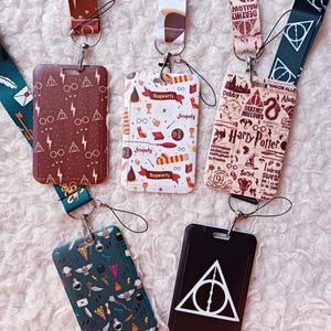 Può includere: Una collezione di cordini con porta badge con vari disegni e testo. I cordini e i porta badge presentano diversi motivi e colori, tra cui bordeaux, bianco e nero. Alcuni porta badge hanno testo come "Hogwarts" e "Harry Potter".